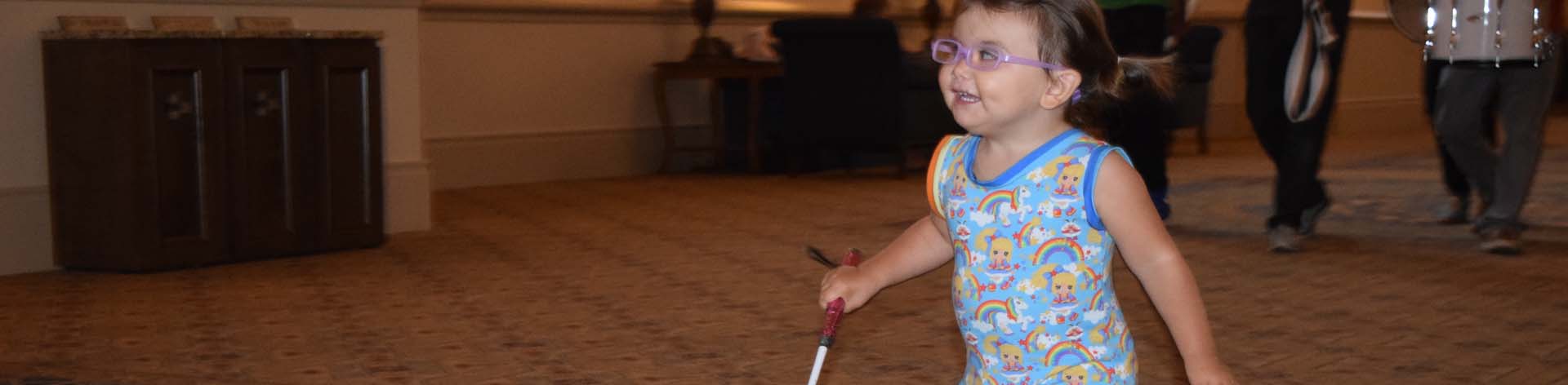 A blind child skips along with her cane in the lead.