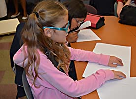 Profile of a blind girl sitting at a table reading a Braille page